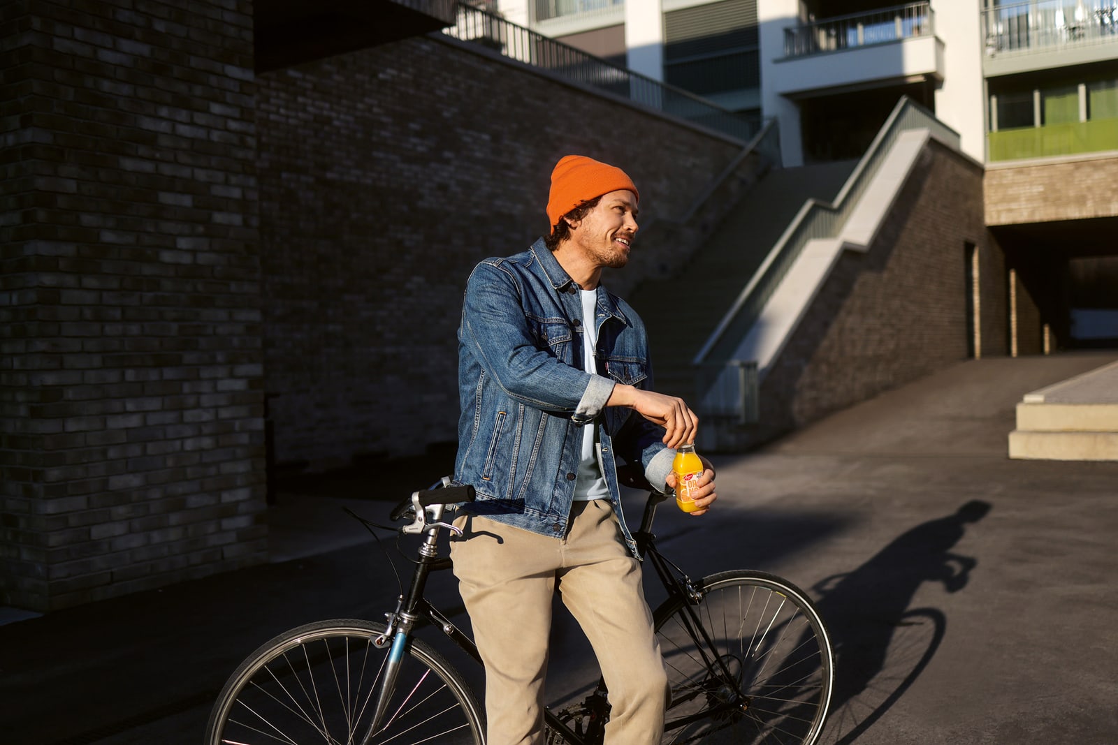 Ein Mann leht an sein Fahrrad an und öffnet einen Orangensaft.
